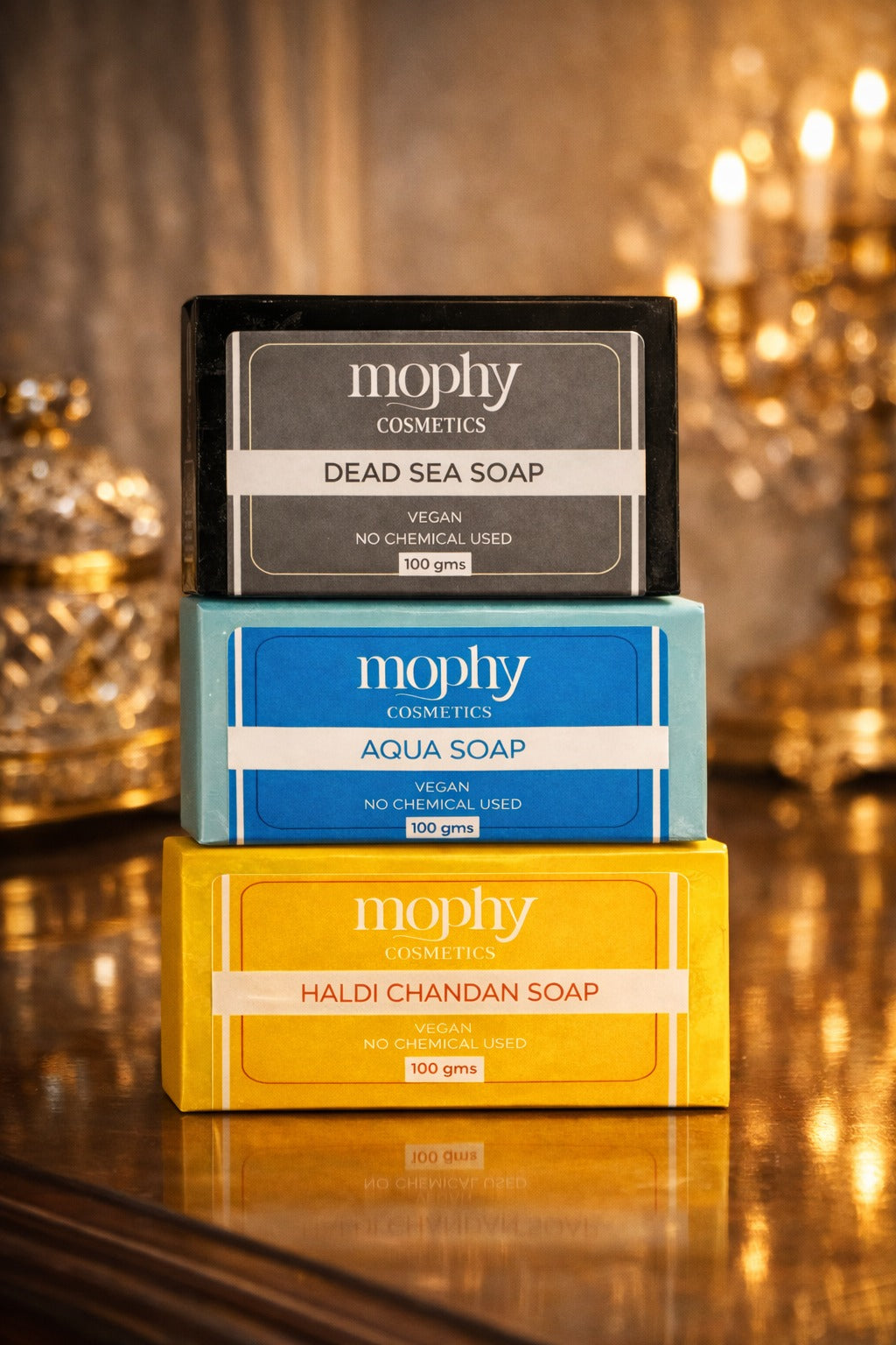 Three mophy Cosmetics soaps stacked on a reflective surface with a blurred decorative background