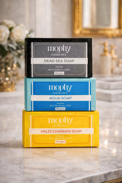 Three Mophy Cosmetics soap bars stacked on a marble surface with a blurred decorative background.